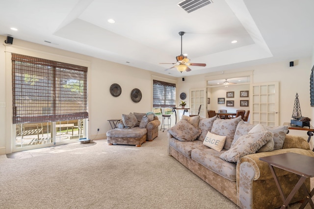 carpeted living room featuring ceiling fan, a tray ceiling, and a wealth of natural light