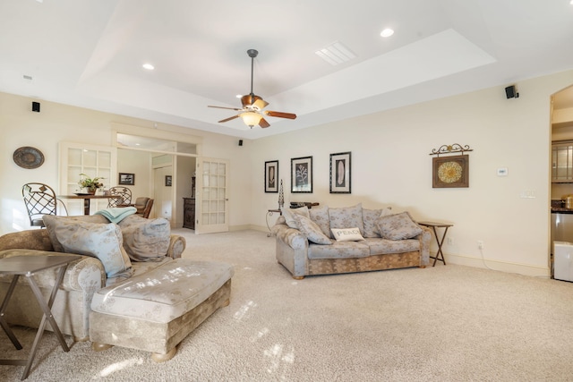 living room with light carpet, ceiling fan, and a raised ceiling