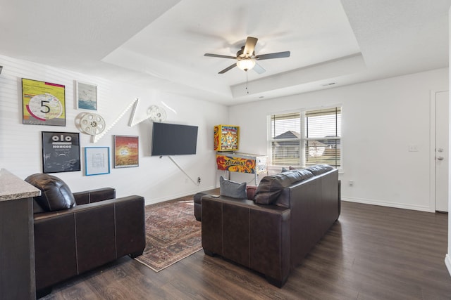 living room featuring ceiling fan, dark wood-type flooring, and a raised ceiling