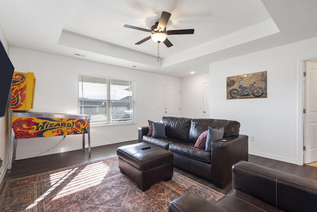 living room featuring dark wood-type flooring, ceiling fan, and a raised ceiling