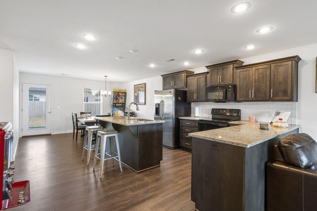 kitchen featuring a breakfast bar area, light stone countertops, black appliances, and dark hardwood / wood-style flooring