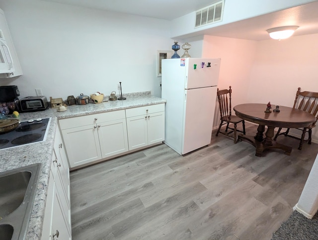 kitchen with stovetop, white cabinetry, white fridge, and light wood-type flooring