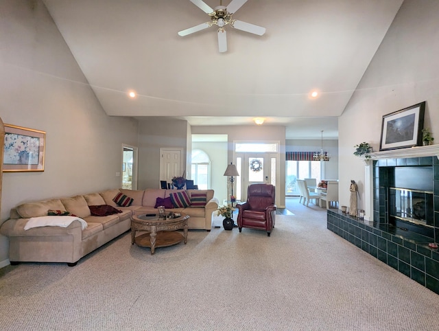 carpeted living room with high vaulted ceiling, a tile fireplace, and ceiling fan with notable chandelier