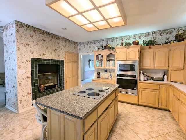 kitchen featuring light brown cabinets, stainless steel appliances, a tile fireplace, light tile patterned flooring, and a center island