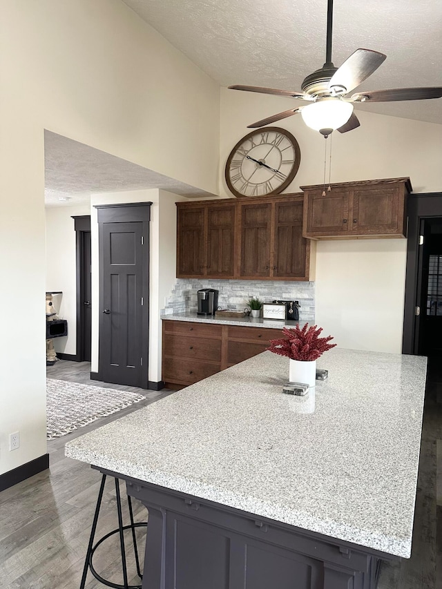 kitchen with backsplash, hardwood / wood-style floors, vaulted ceiling, a textured ceiling, and ceiling fan