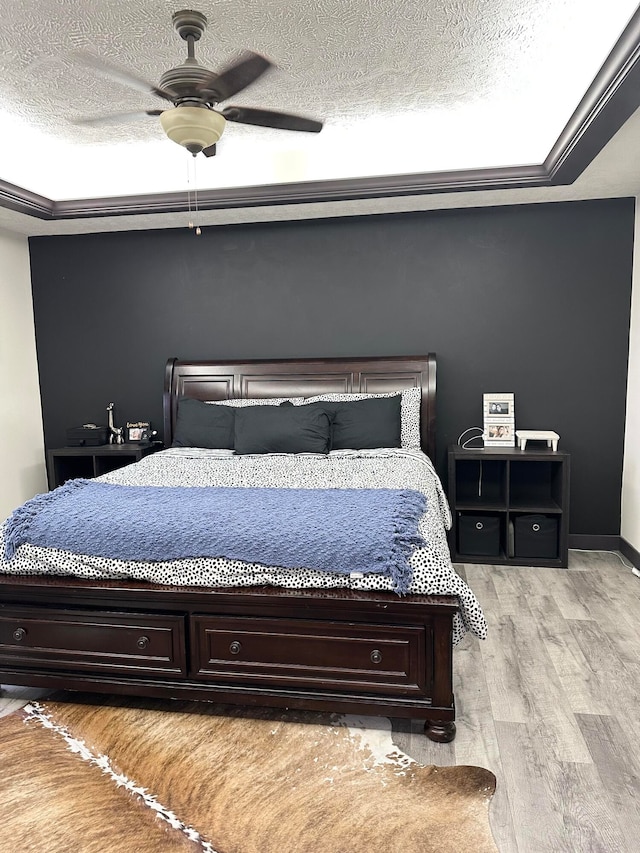 bedroom with a tray ceiling, a textured ceiling, light wood-type flooring, and ceiling fan