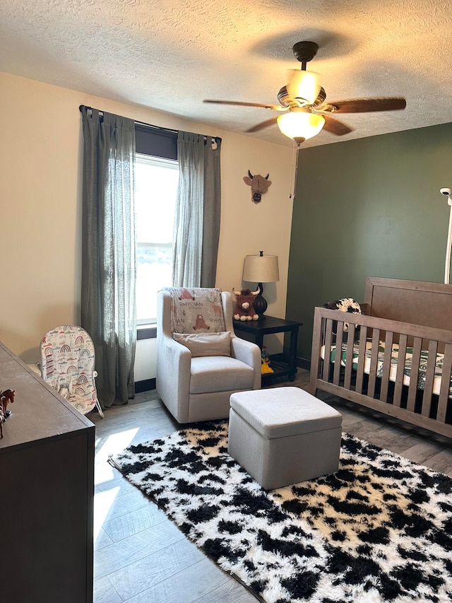 bedroom with a textured ceiling, a crib, and ceiling fan