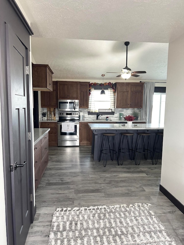 kitchen featuring appliances with stainless steel finishes, wood-type flooring, a textured ceiling, ceiling fan, and a breakfast bar area