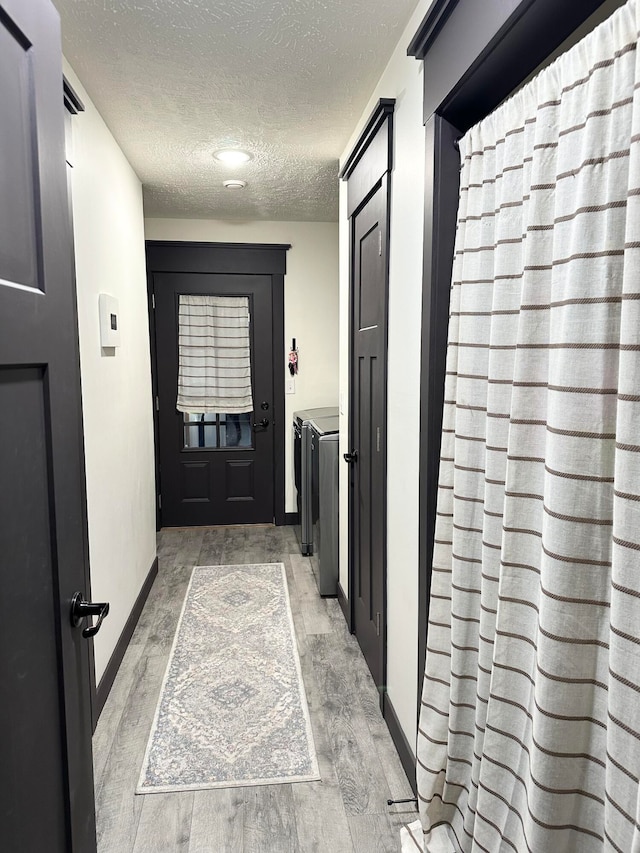 doorway with washing machine and dryer, a textured ceiling, and light hardwood / wood-style flooring