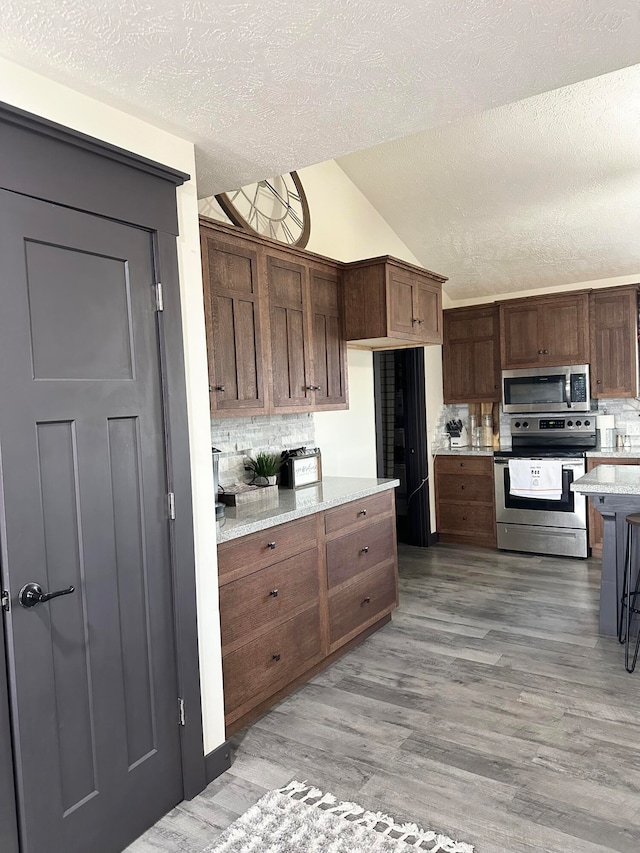 kitchen featuring lofted ceiling, stainless steel appliances, backsplash, hardwood / wood-style floors, and a textured ceiling