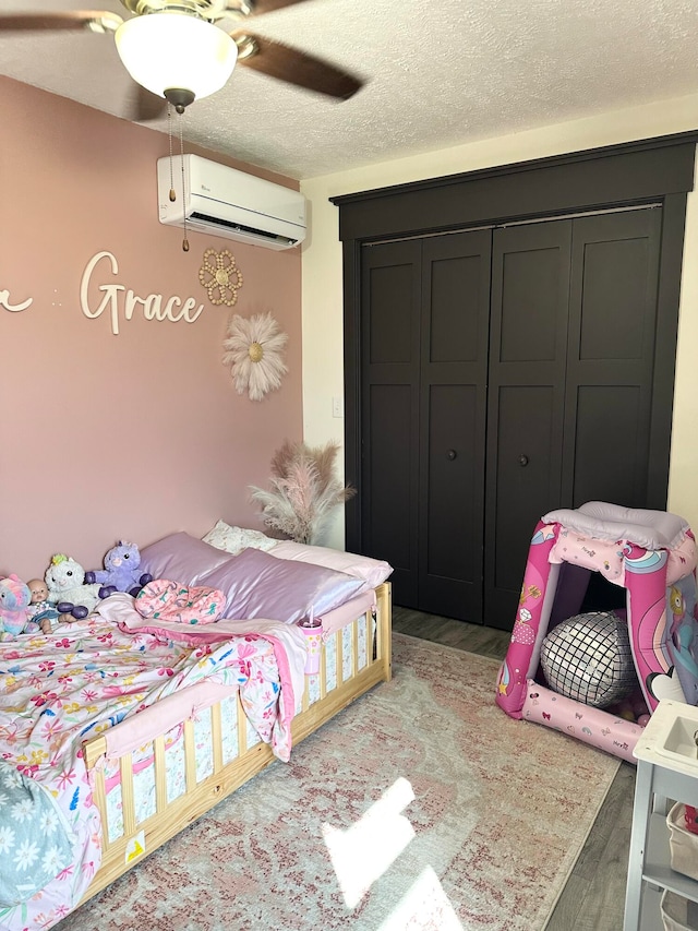 bedroom featuring ceiling fan, a wall mounted AC, a textured ceiling, and light hardwood / wood-style floors