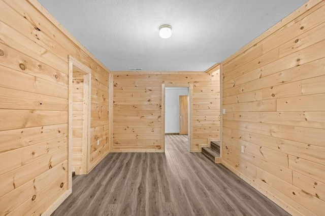 unfurnished room with dark wood-style flooring, wood walls, and a textured ceiling