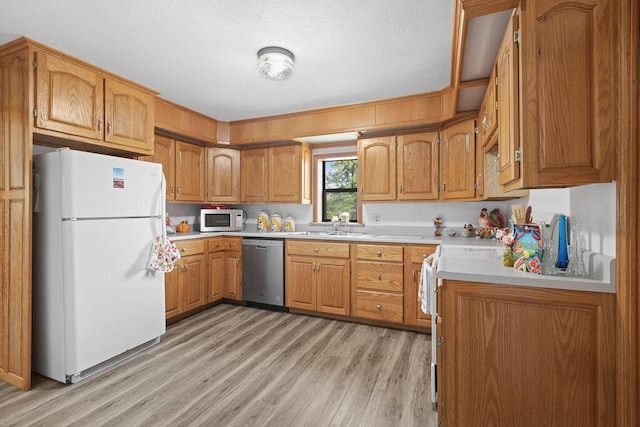 kitchen featuring brown cabinets, light countertops, a sink, light wood-style floors, and stainless steel appliances
