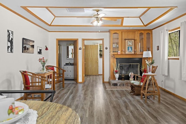 living area with visible vents, ornamental molding, a glass covered fireplace, wood finished floors, and ceiling fan