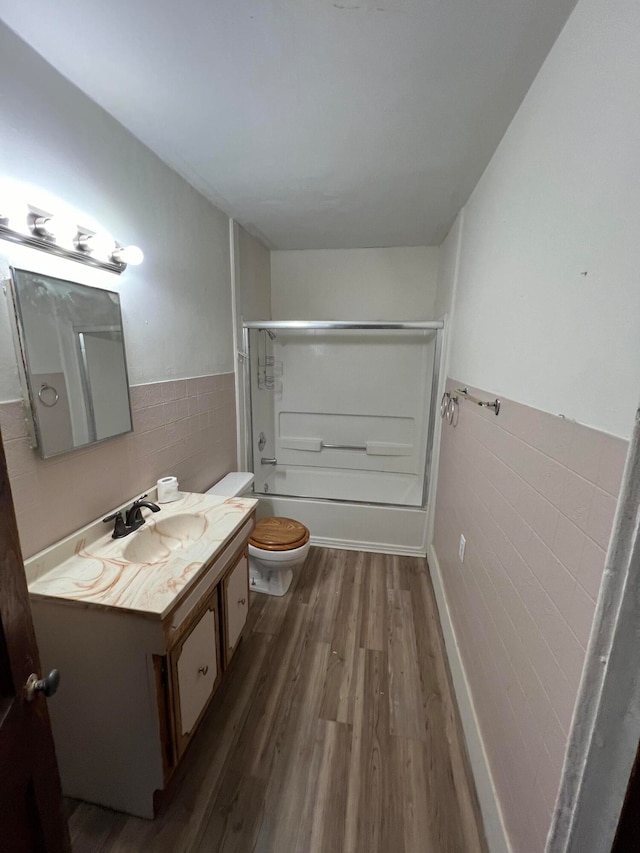 full bathroom featuring combined bath / shower with glass door, wood-type flooring, tile walls, toilet, and vanity