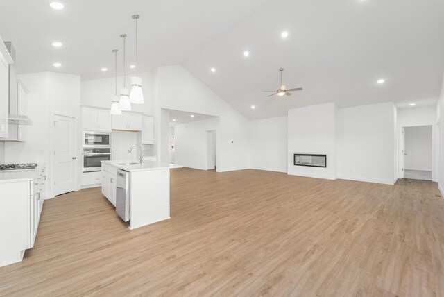 kitchen with light hardwood / wood-style flooring, stainless steel appliances, a center island with sink, white cabinetry, and high vaulted ceiling