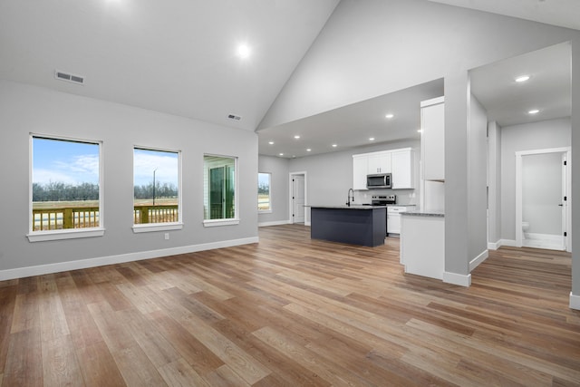 unfurnished living room with sink, high vaulted ceiling, and light wood-type flooring