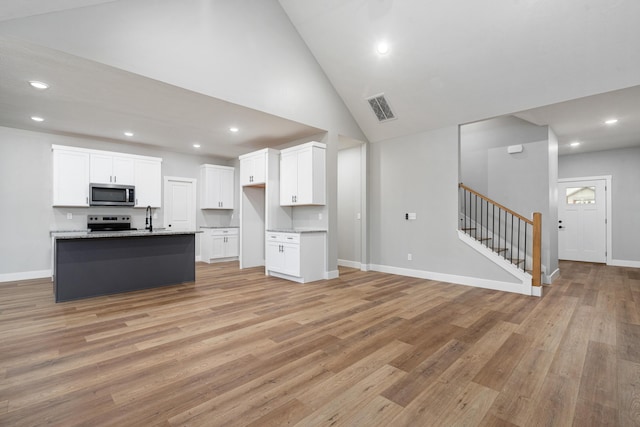 kitchen featuring white cabinetry, light hardwood / wood-style floors, stainless steel appliances, light stone countertops, and a center island with sink