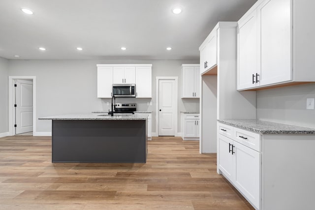 kitchen featuring light stone counters, light wood-type flooring, appliances with stainless steel finishes, an island with sink, and white cabinets