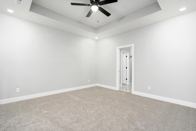 carpeted empty room featuring ceiling fan and a raised ceiling