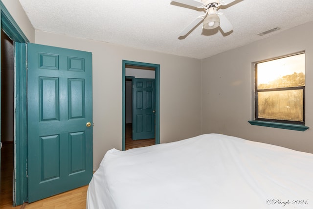 bedroom with light hardwood / wood-style flooring, a textured ceiling, and ceiling fan