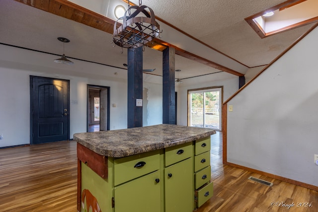 kitchen with a textured ceiling, a center island, a skylight, light hardwood / wood-style floors, and green cabinets