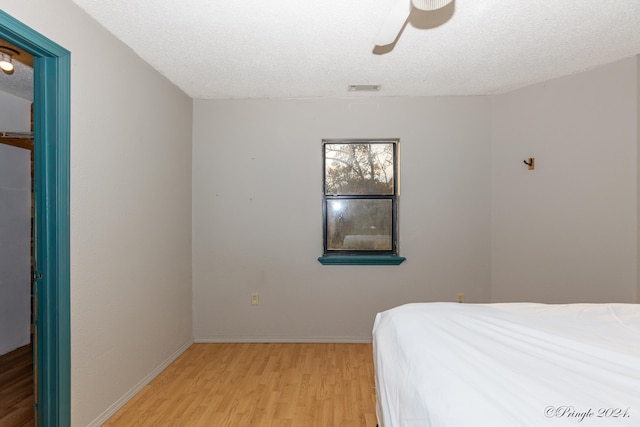 bedroom featuring light hardwood / wood-style flooring, a textured ceiling, and ceiling fan