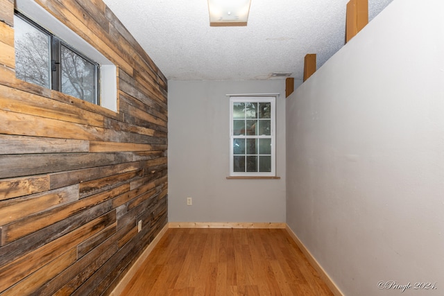 unfurnished room featuring light hardwood / wood-style floors, a textured ceiling, and wooden walls