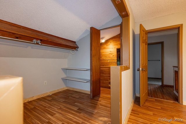 interior space featuring lofted ceiling, a textured ceiling, hardwood / wood-style flooring, and wood walls