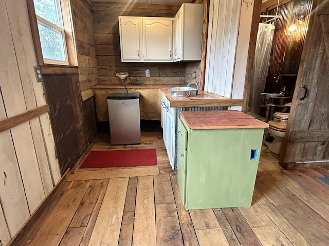 kitchen with wood walls, light wood-type flooring, a kitchen island, and white cabinets