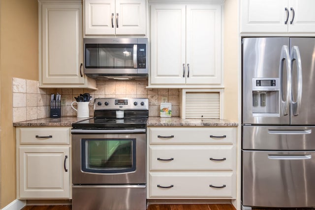 kitchen with appliances with stainless steel finishes, white cabinetry, light stone counters, and backsplash