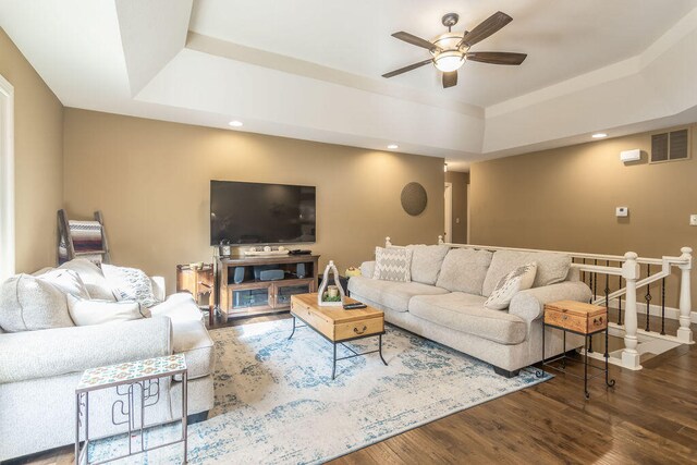 living room with ceiling fan, a raised ceiling, and dark hardwood / wood-style flooring