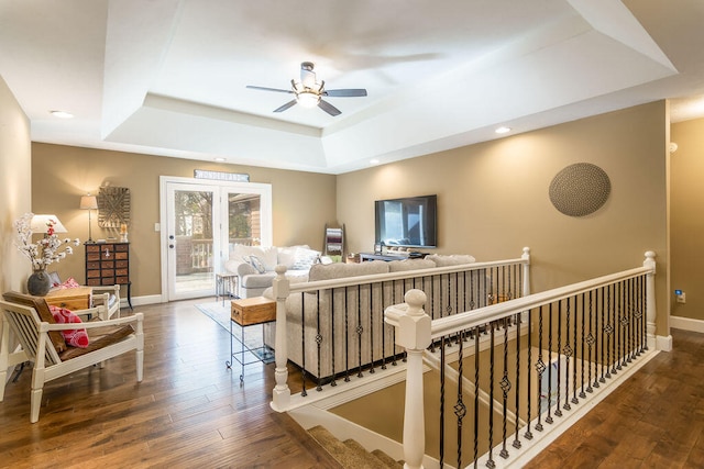 living room featuring dark hardwood / wood-style flooring, ceiling fan, and a raised ceiling