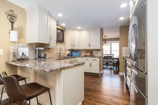 kitchen featuring kitchen peninsula, stainless steel appliances, pendant lighting, white cabinets, and dark wood-type flooring