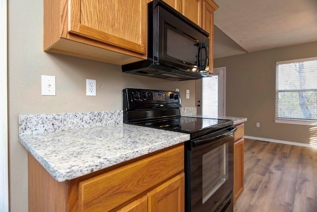 kitchen with light stone counters, black appliances, and dark wood-type flooring