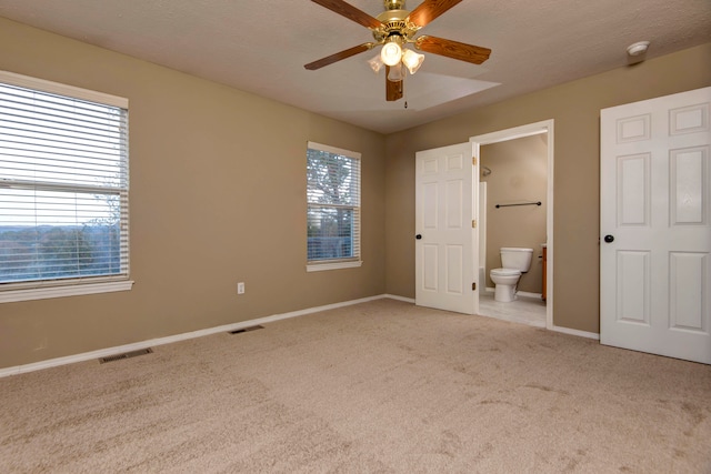 unfurnished bedroom featuring a textured ceiling, ensuite bath, light colored carpet, and ceiling fan