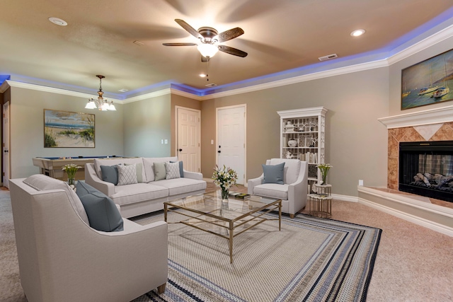 carpeted living room with a tile fireplace, crown molding, and ceiling fan with notable chandelier