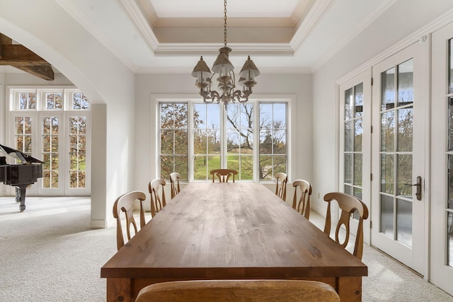 dining space featuring crown molding, light carpet, an inviting chandelier, and a raised ceiling