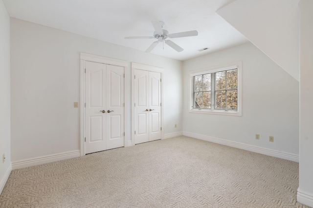 unfurnished bedroom featuring multiple closets, light colored carpet, and ceiling fan