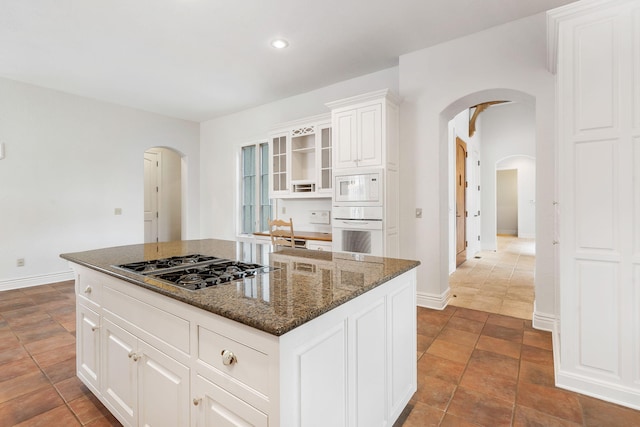 kitchen featuring a kitchen island, dark tile patterned flooring, dark stone counters, white cabinetry, and white appliances