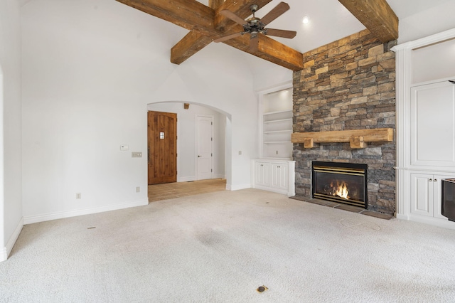 unfurnished living room featuring beamed ceiling, light carpet, a fireplace, and ceiling fan