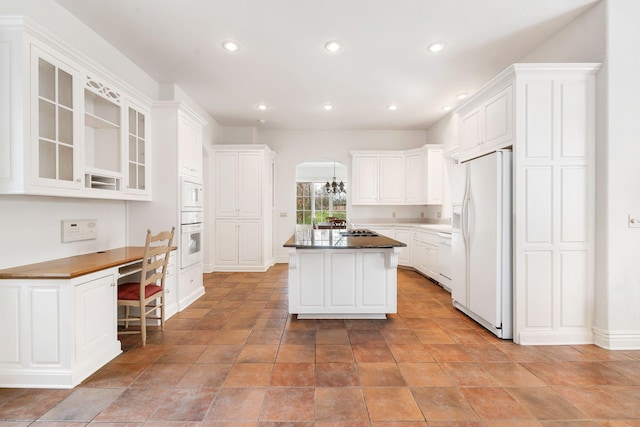 kitchen with white appliances, a kitchen island, built in desk, a kitchen breakfast bar, and white cabinets