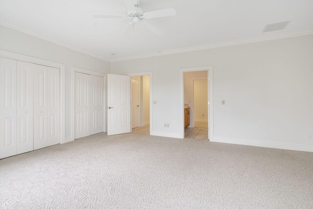 unfurnished bedroom featuring multiple closets, light carpet, ornamental molding, ensuite bathroom, and ceiling fan