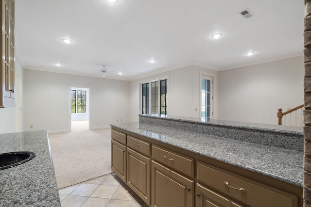 kitchen featuring dark stone countertops, crown molding, light colored carpet, and ceiling fan