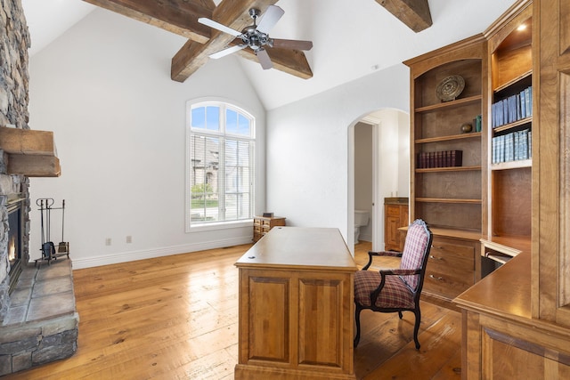 office space with a stone fireplace, lofted ceiling with beams, ceiling fan, and light hardwood / wood-style floors