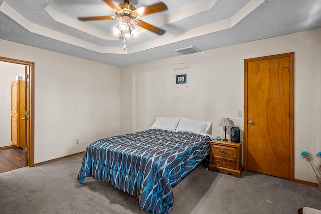 carpeted bedroom with a raised ceiling, ensuite bath, ceiling fan, and a textured ceiling