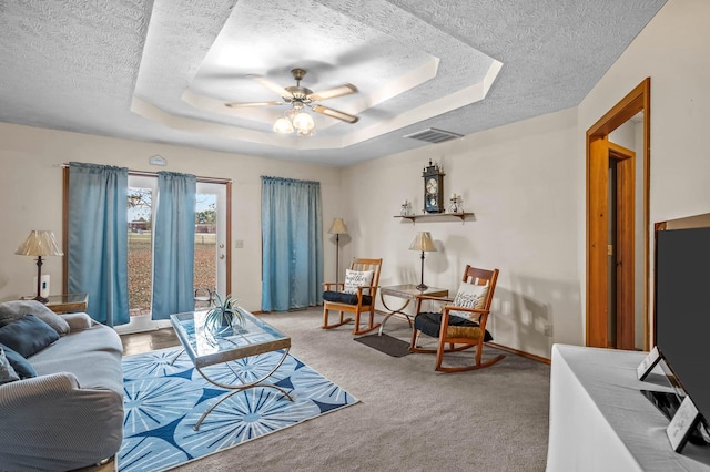 carpeted living room with a textured ceiling, a tray ceiling, and ceiling fan