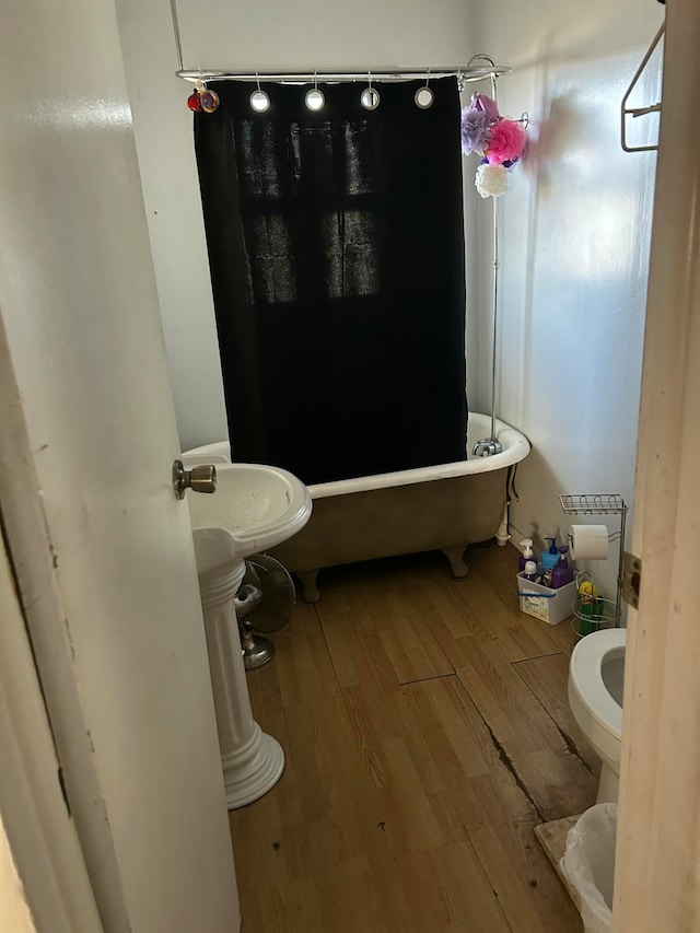 bathroom with a bath, toilet, and wood-type flooring