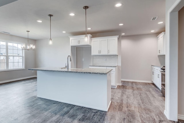 kitchen featuring sink, a center island with sink, white cabinetry, and decorative light fixtures