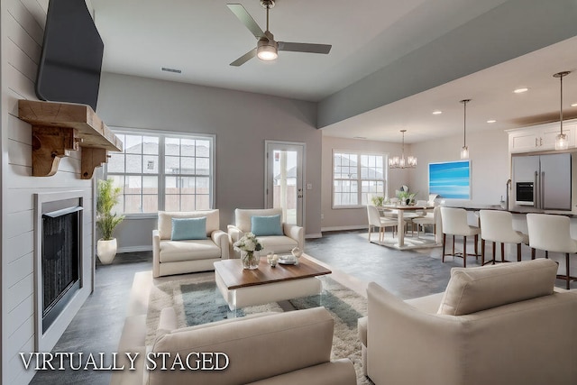 living room featuring ceiling fan with notable chandelier, plenty of natural light, and concrete flooring